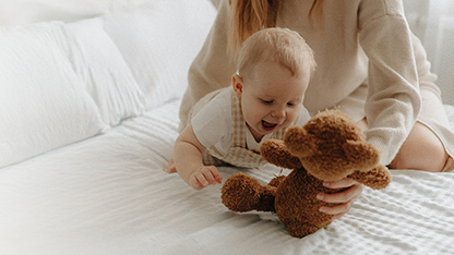 Un bébé qui joue avec un ours en peluche sous la supervision de sa maman.