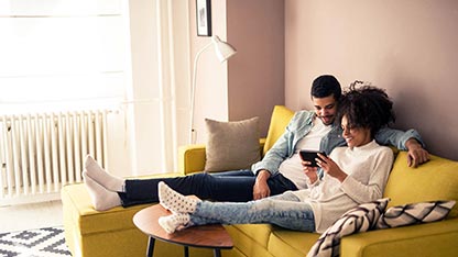 Un couple se détend ensemble sur un canapé en regardant une vidéo sur un téléphone portable.