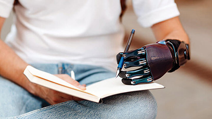 Une personne écrit dans un cahier avec une main prothétique tenant le stylo.