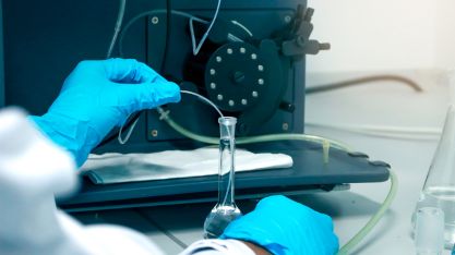Main de chercheur avec gants de protection chimique bleus utilisant une fiole jaugée pour réaliser une expérience visant à déterminer les niveaux de métaux lourds dans des solutions par ICP (spectromètre à plasma inductif).